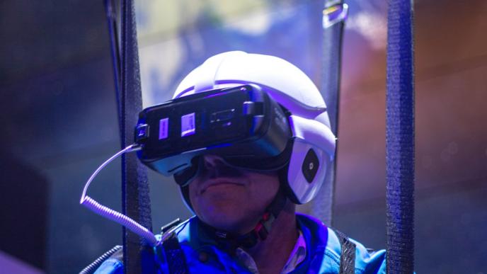 user suspended in air by braces in a safety suit and helmet that has a VR headset on with an image of earth in the backgroun