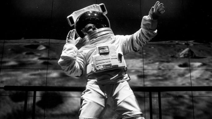 black and white image of user in an astronaut space suit holding their hands up in the air with the moon surface and earth in space in the background