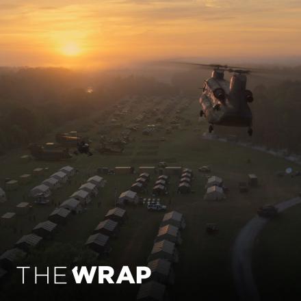 Helicopters flying towards a sunset over a military encampment with the logo for the The Wrap in the bottom left corner.