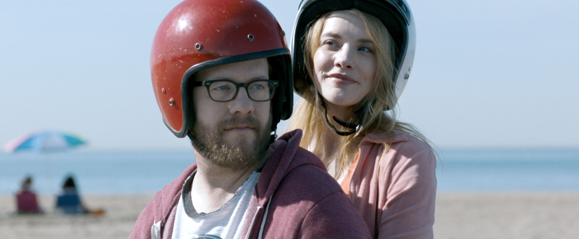 A man and a woman sit on a moped together, wearing helmets