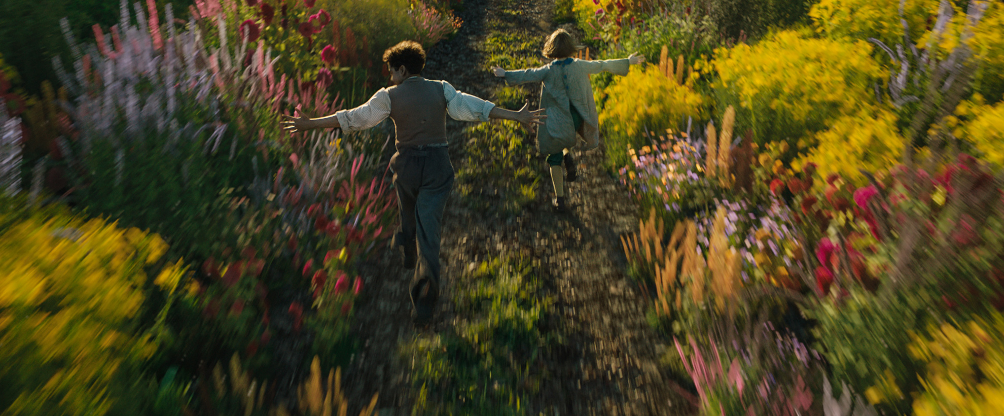 Two children run through a flowering garden