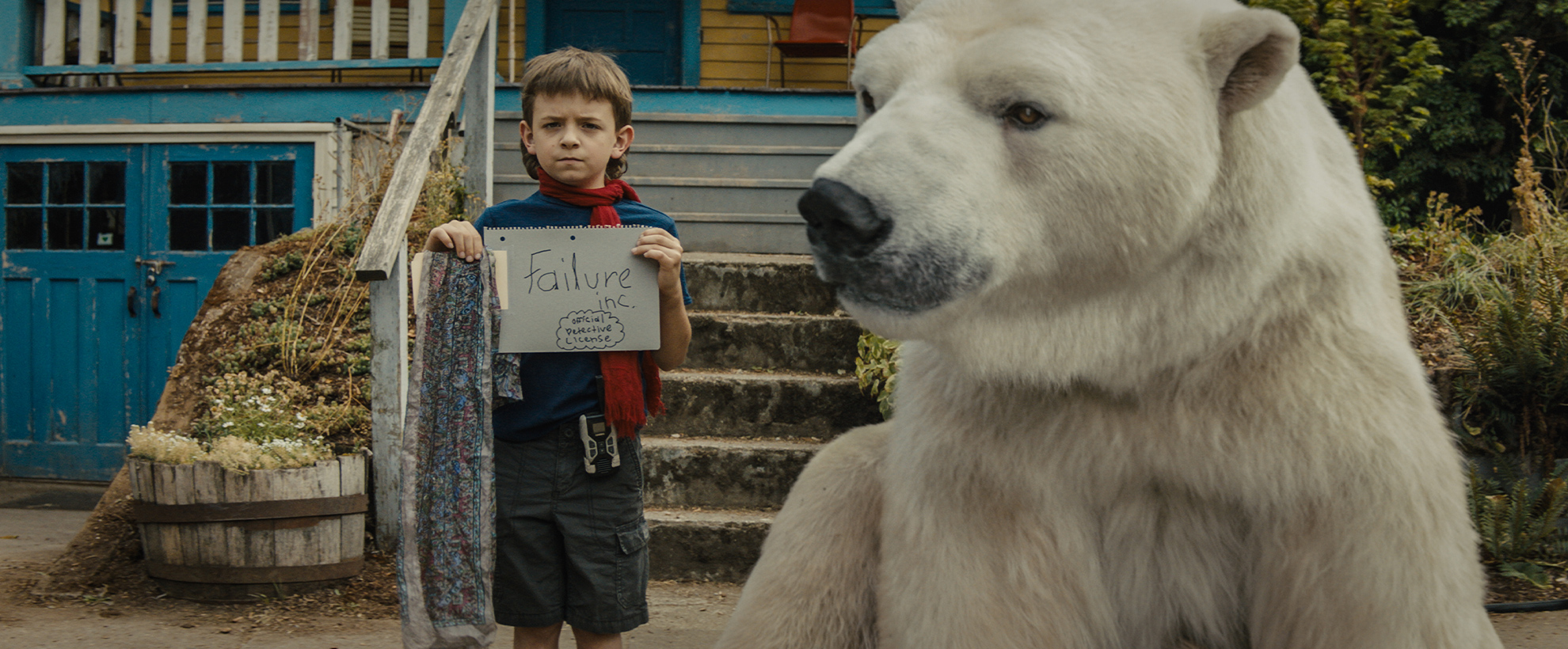 A young boy stands on the pavement in front of his house with a large polar bear sat next to him