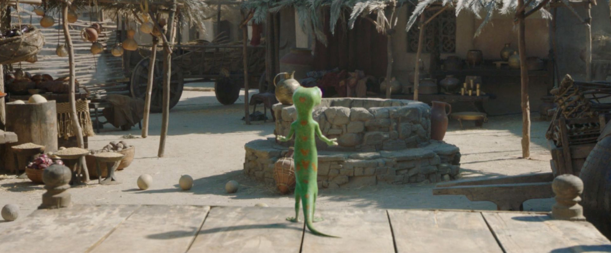 The GEICO gecko stood in front of a well in a market area.