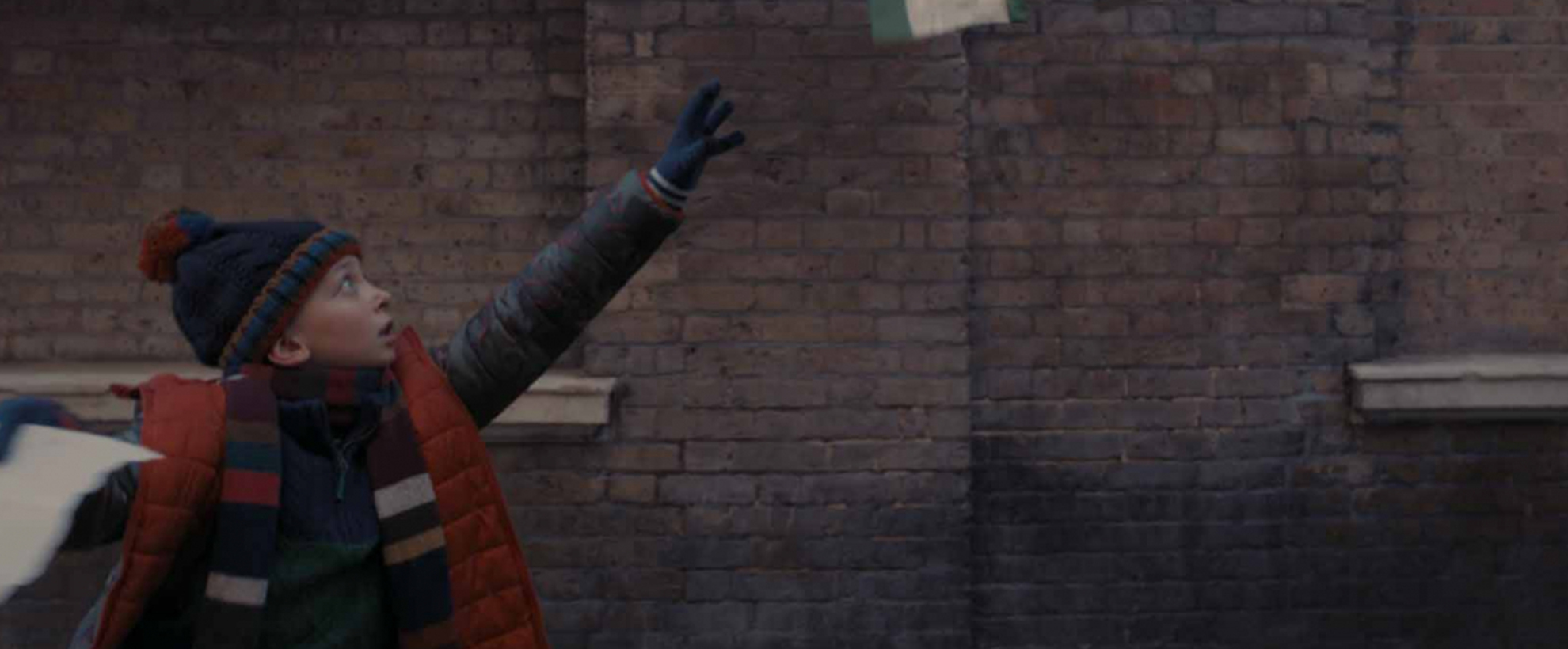 A young boy in winter clothing reaches up as his papers fly away