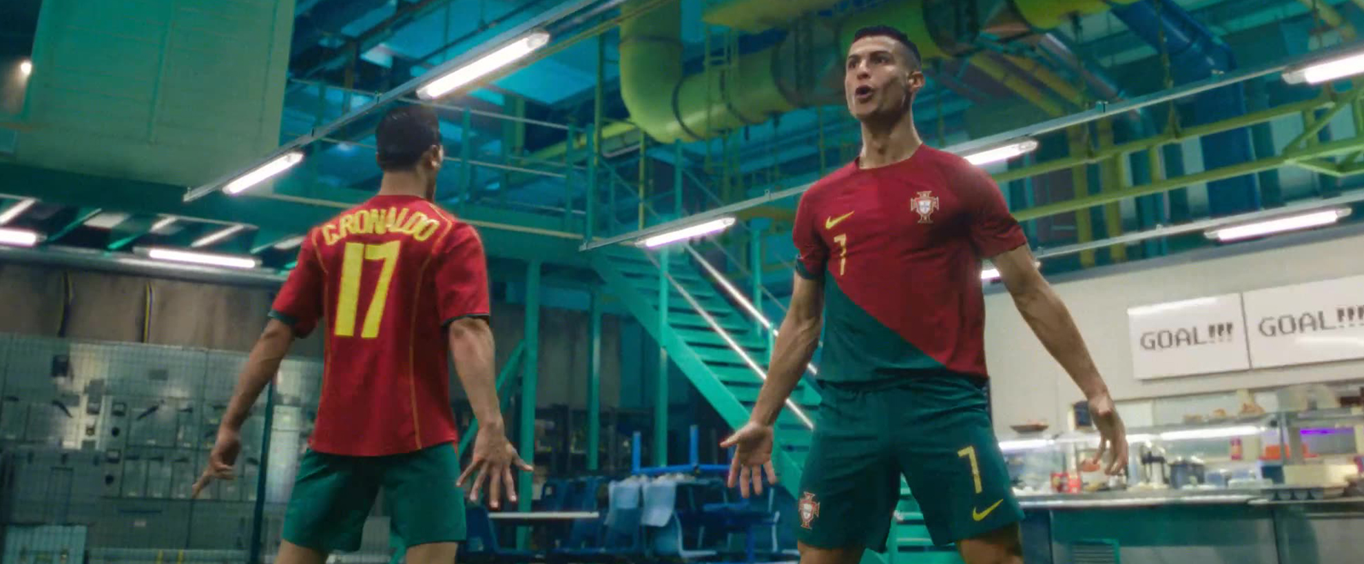 Two football players face each other in a warehouse setting, celebrating a goal