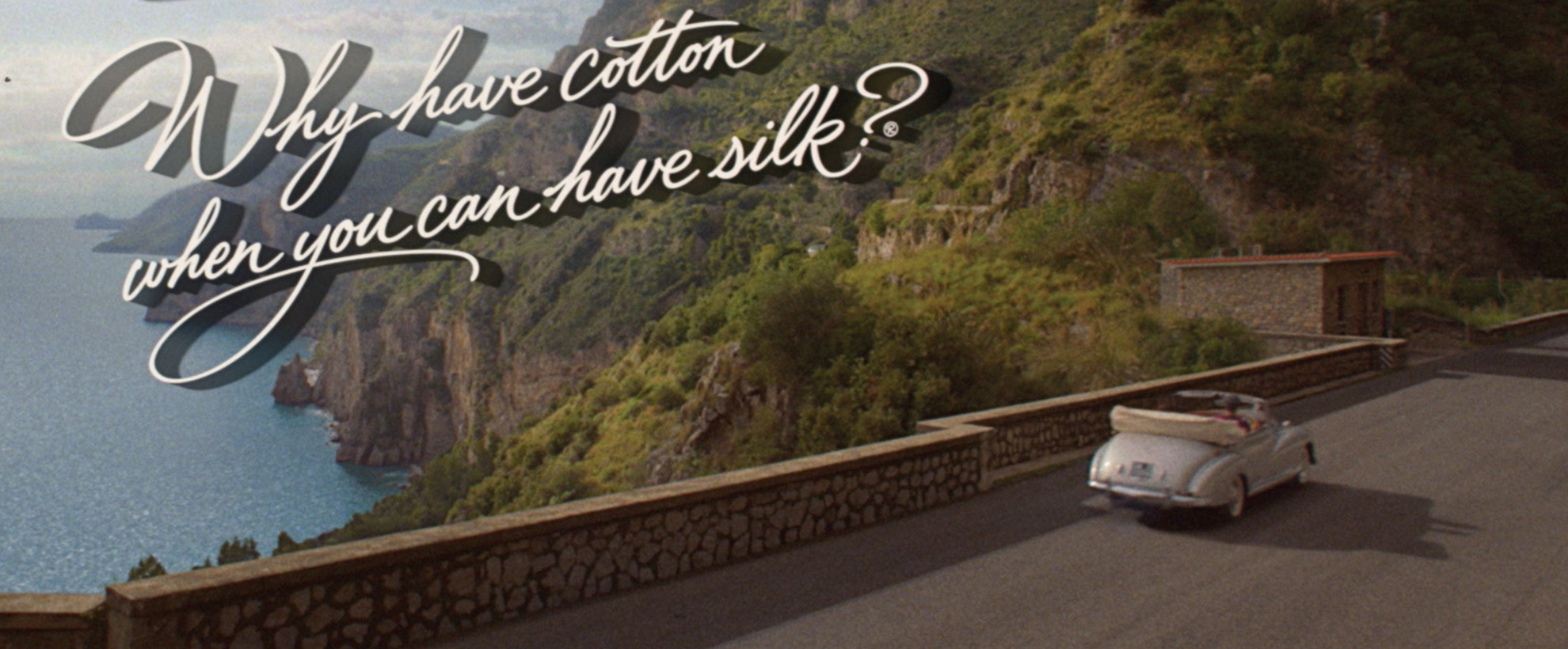 The phrase 'Why have cotton when you can have silk' is written across a shot of the Italian coast with a vintage convertible car overlooking the view