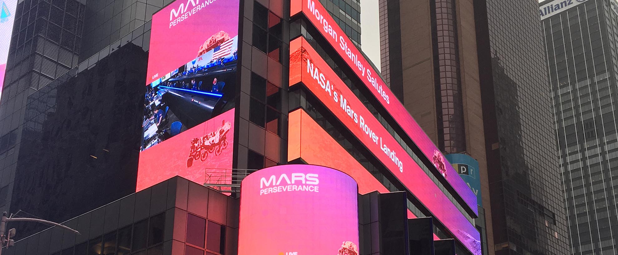 Billboard screens on the side of city buildings say "Morgan Stanley salutes NASA's Mars Rover Landing"