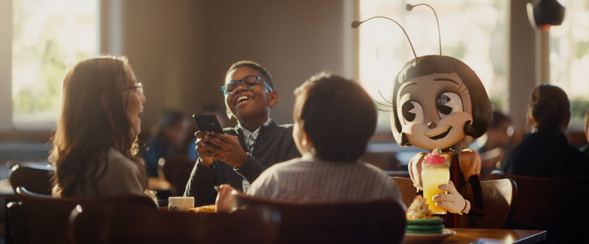 A character from the film IF sits at a table in an IHOP restaurant with a group of children in suits