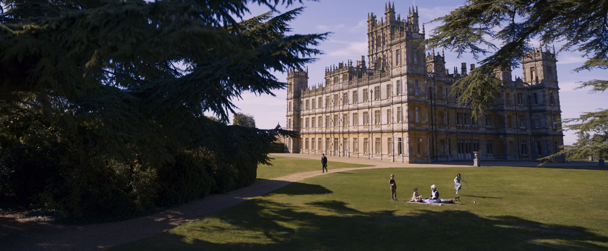 An exterior shot of Downton Abbey, with people sitting outside on the lawns