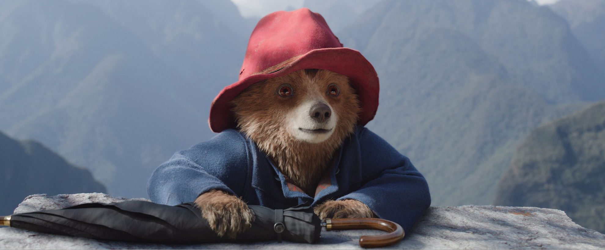 In Paddington in Peru, a CGI Paddington Bear climbs up over a ledge, wearing a blue duffle coat and red hat