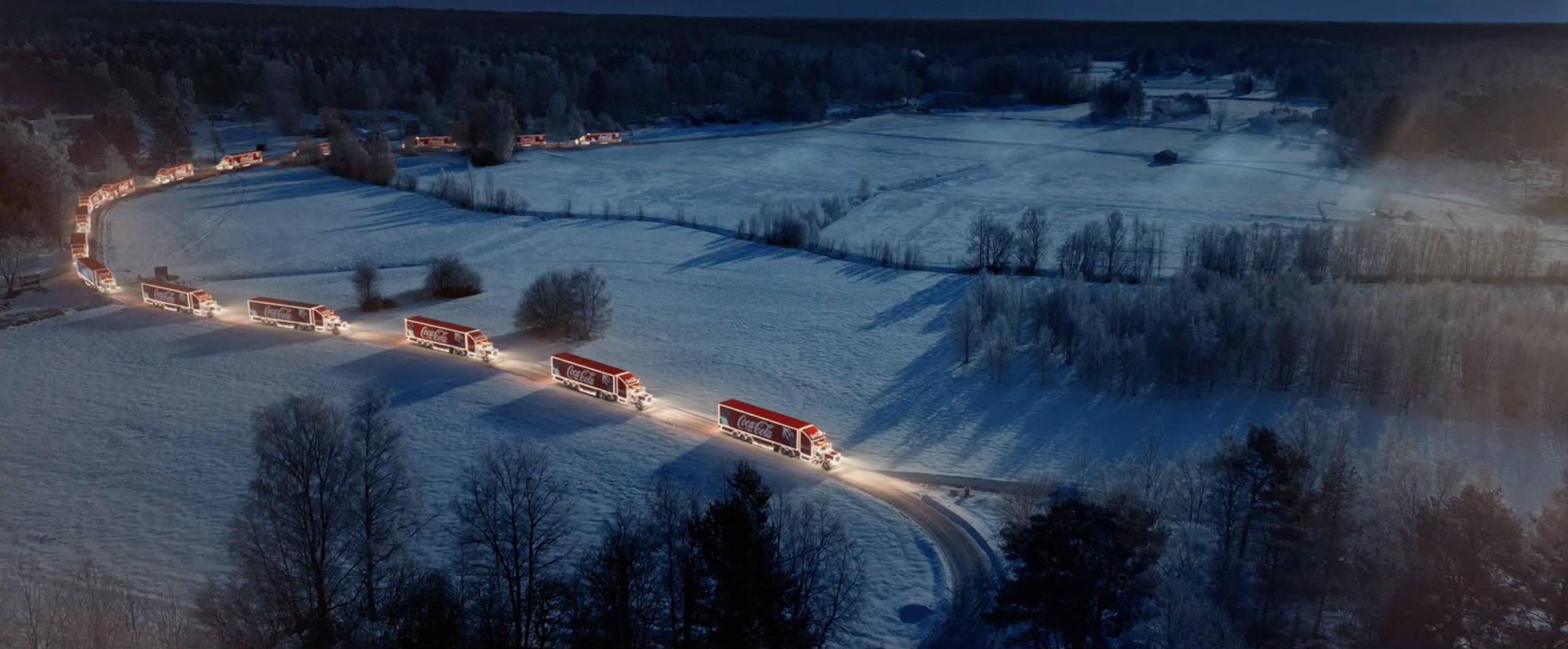 A fleet of red lit up Coca Cola trucks driving down a lane in a vfx snowy backdrop.