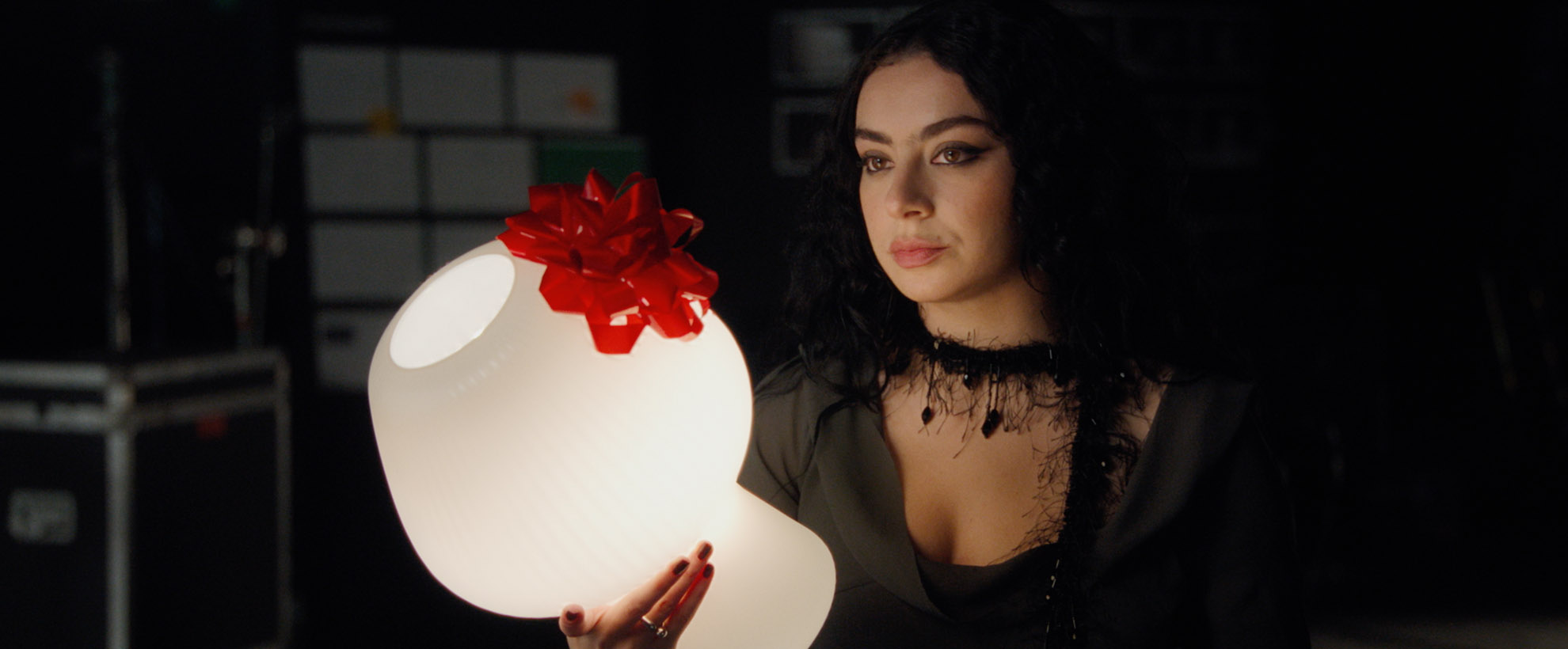 Charli xcx holds a lamp with a red bow on it