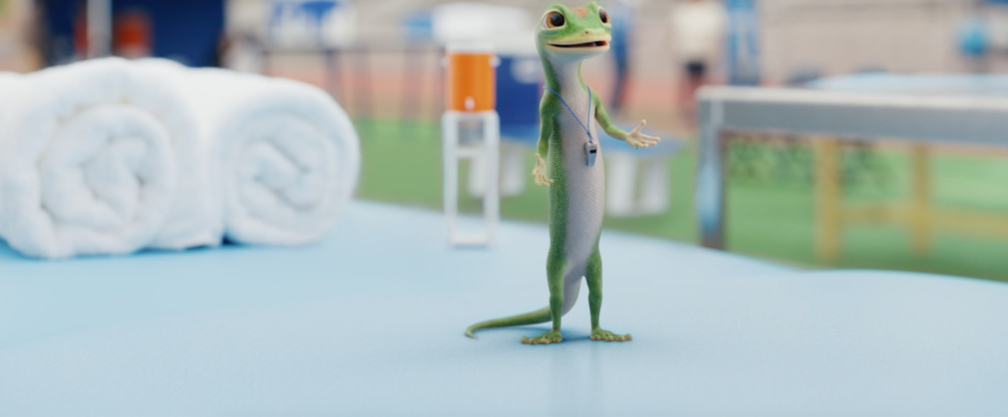 The animated GEICO Gecko stands on a training table on a football field