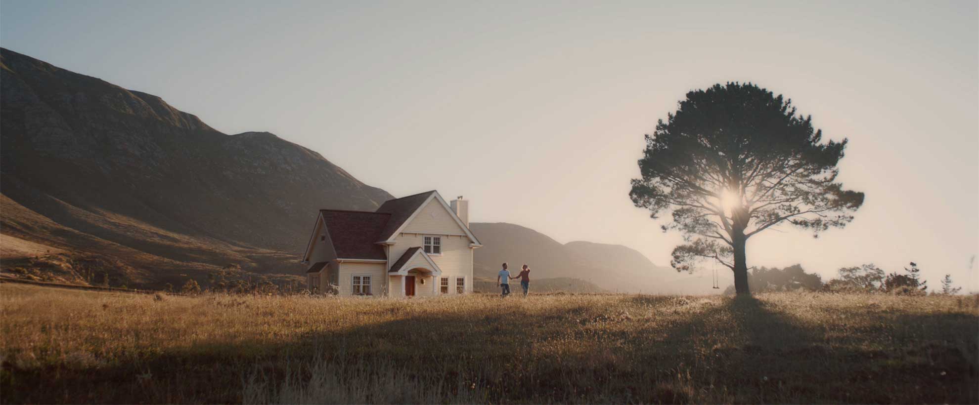 Sunny, calm landscape with mountains in the distance and a house and tree in the forefront