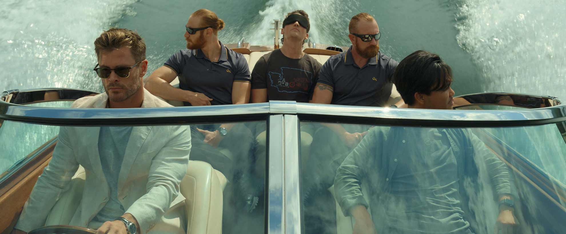 Chris Hemsworth drives a speedboat with three people in the back, one blindfolded