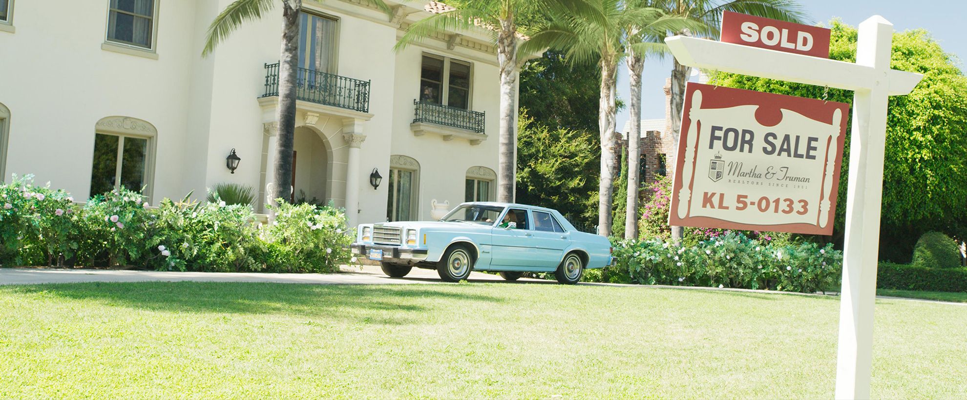 A blue car parked in front of a white house, with a "sold" sign in the front garden