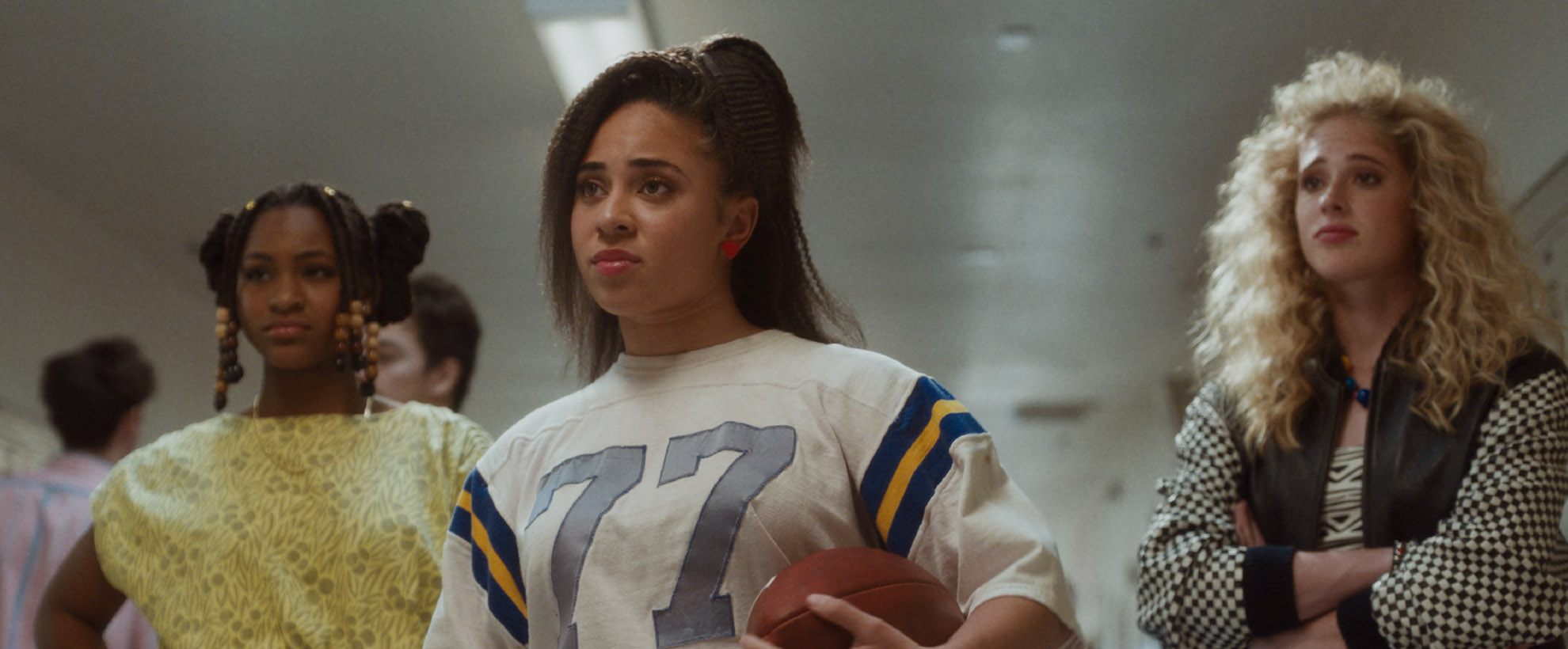 A female flag football player in 80s attire stands in a high school hallway with her friends