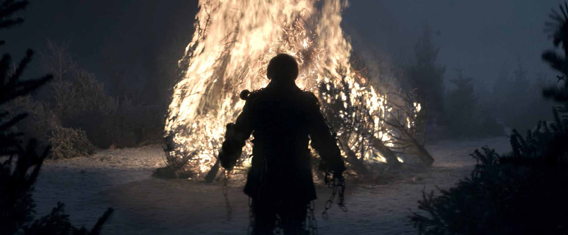 back view of scrooge from a christmas carol standing in front of a large burning bonfire