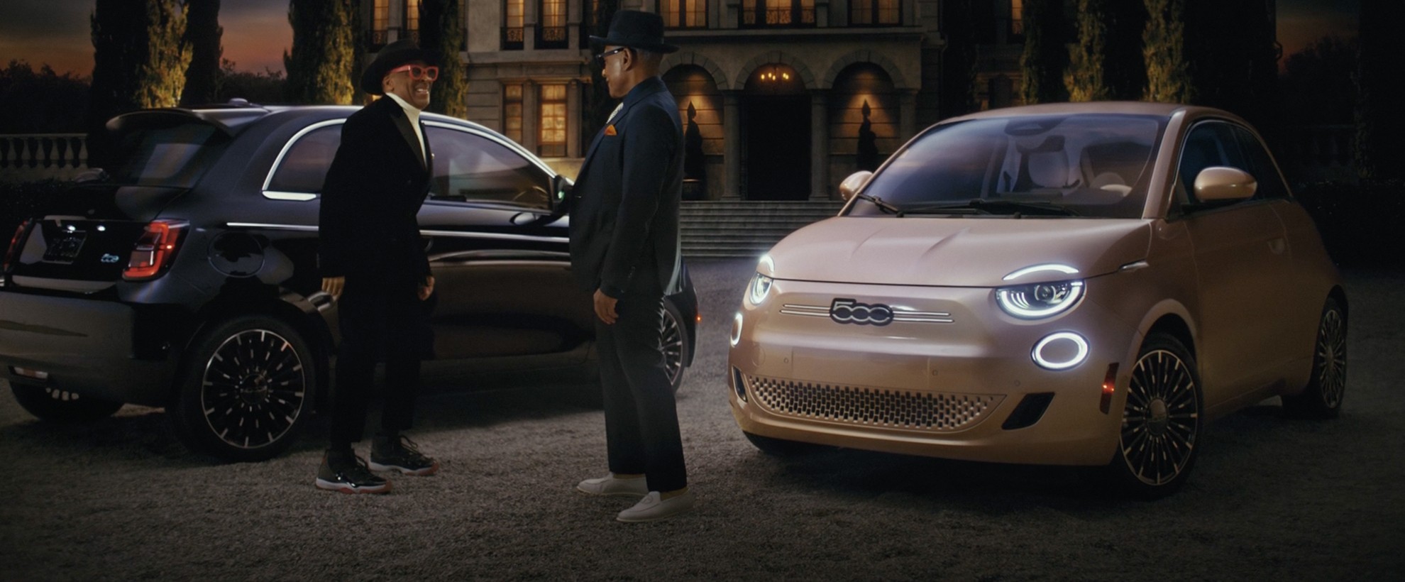 Spike Lee and Giancarlo Esposito next two two Fiat cars, outside of a mansion