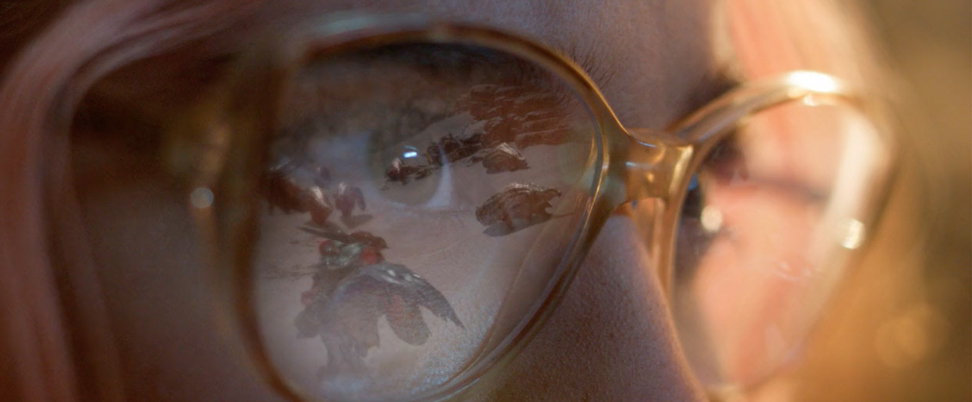 A close up on a woman's face as she plays Monster Hunter Wilds, the reflection of the game play in her glasses