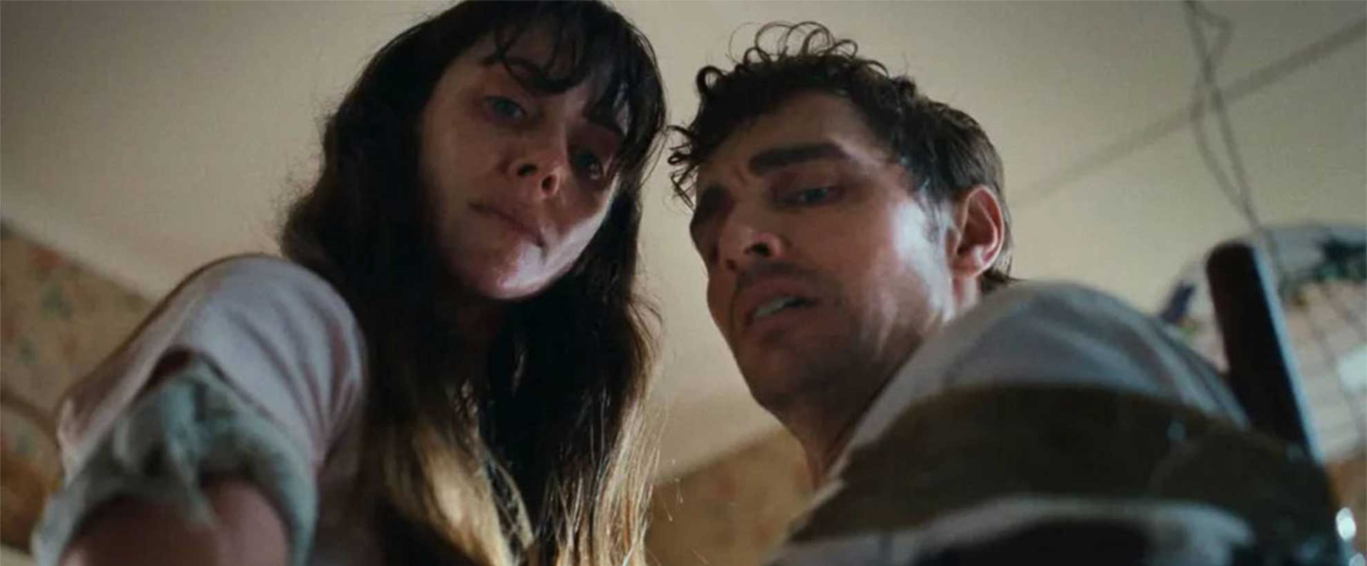 A man and a woman stand close together, both looking down. A still frame from the film Together, starring Dave Franco