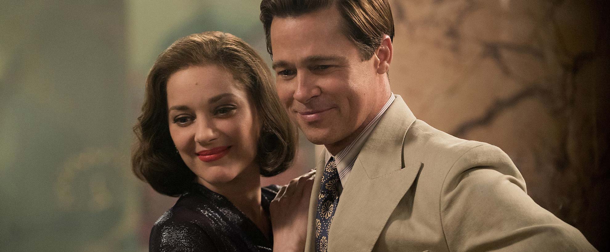 A man and a woman stand close together, both looking down. 