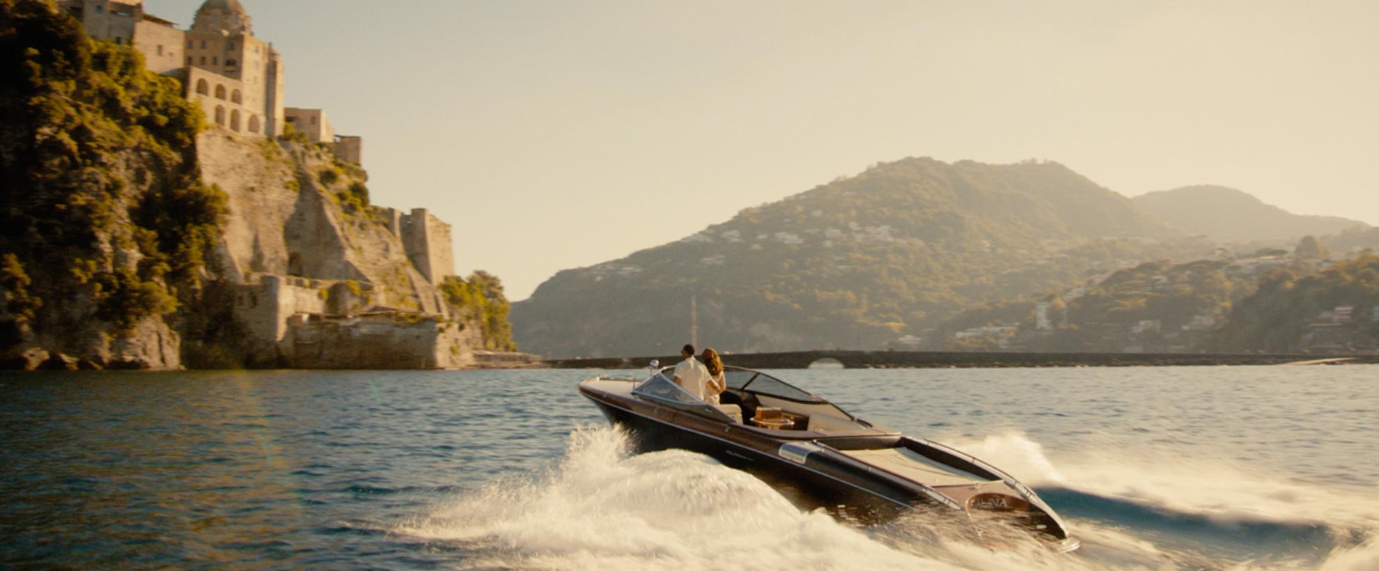 A frame from The Thomas Crown Affair showing Michael B. Jordan and a female co-star on a speedboat, sailing towards a mediterranean coastal town.
