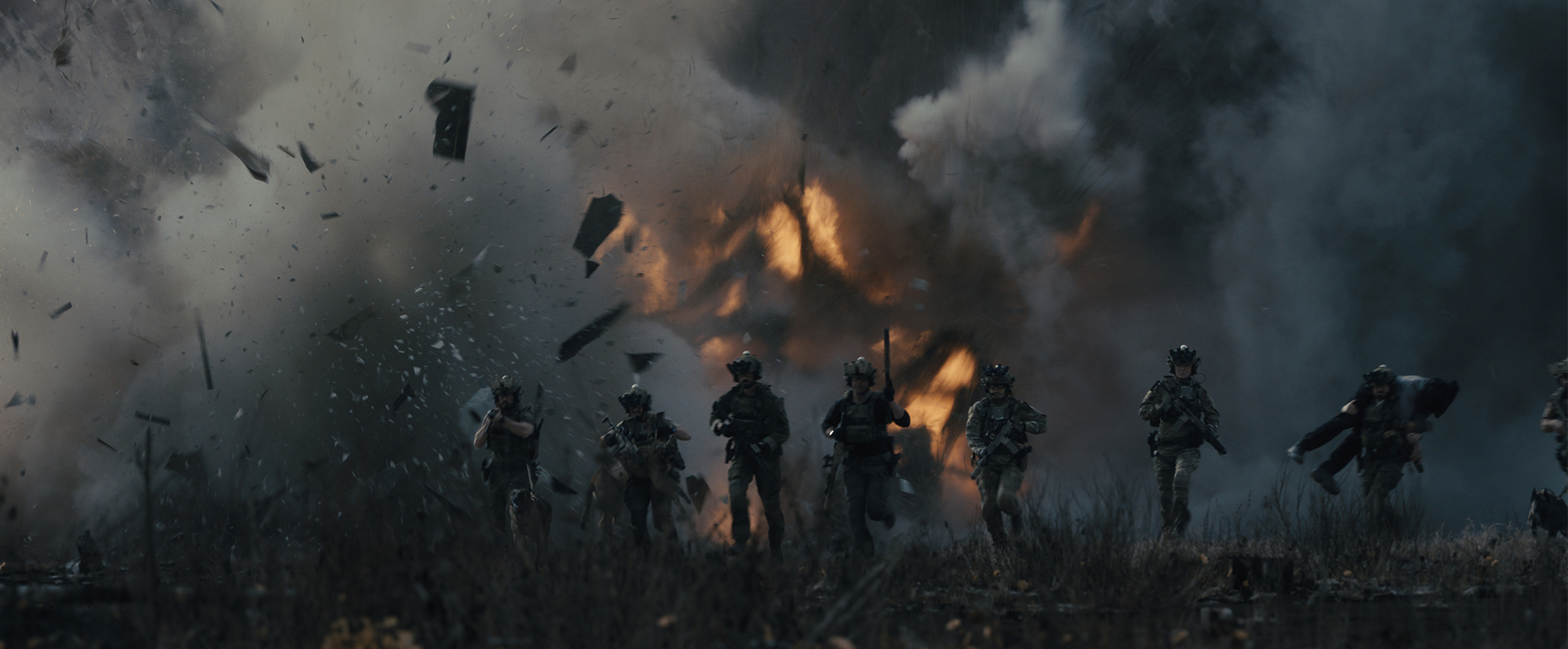 Soliders on a battlefield running forward as an explosion erupts behind them.