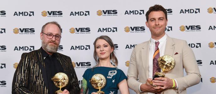 Three people stand on the red carpet at the VES awards, holding golden awards