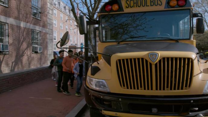 front facing image of kids queuing to get on a yellow school bus