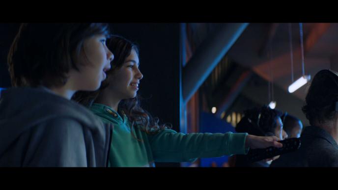 two children looking into the distance. one of them is holding a tv remote and pointing it towards a screen