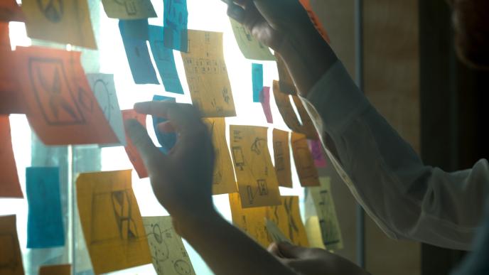 an illuminous white board that is covered in post-it notes as two people are reaching to them
