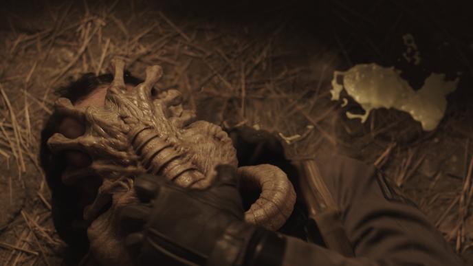 a facehugger alien creature attached to a man's face as he tries to yank it off of him