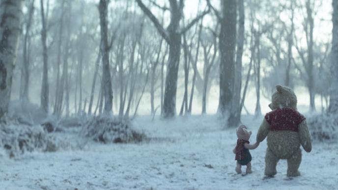back view of piglet and winnie the pooh walking while holding hands in a snowy forest