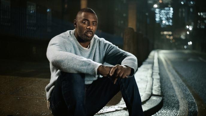 idris elba sitting on a side curb 