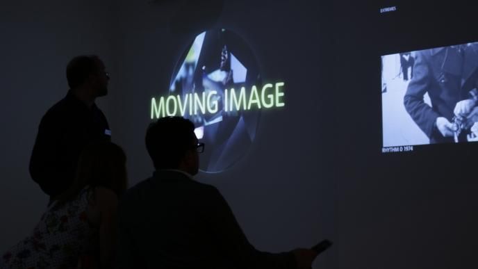 side view of three people watching an exhibition that is projected on the walls