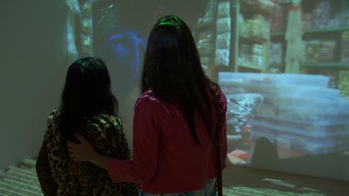 back view of two women watching an exhibition that is projected onto a wall
