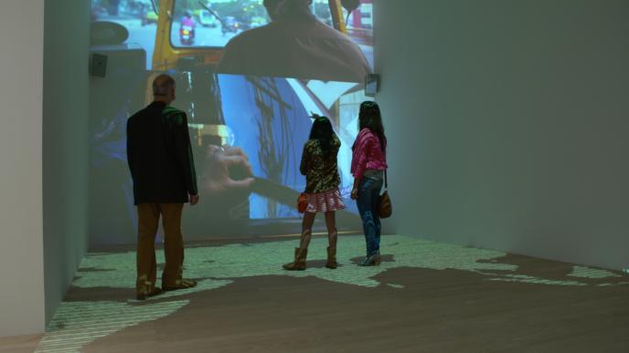 back view of three people standing in front of a wall that has an exhibition projected across its walls