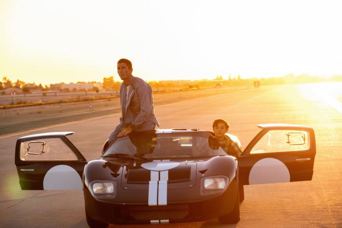 one person sitting on the roof of a ferrari car as a child sits inside. the doors of the car are open. the sun is setting in the background