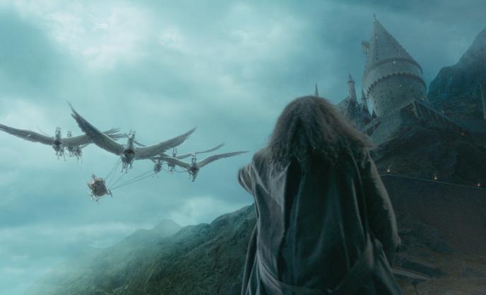 back view of hagrid the giant from harry potter pointing to the sky as pegasus and a chariot descend from the sky. the hogwarts building is in the background on the right