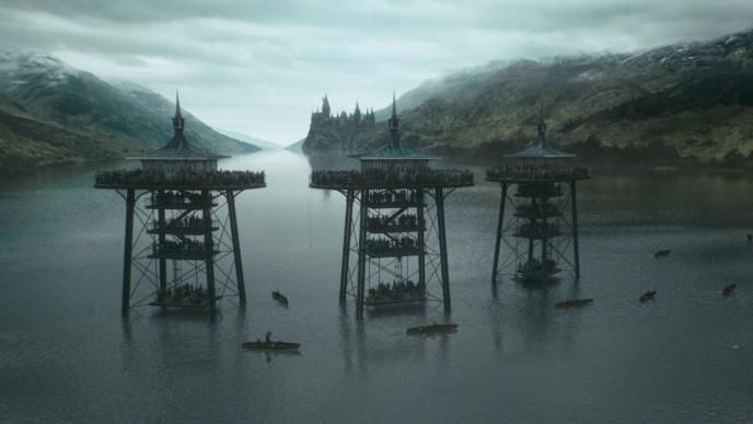 three pillars full of spectators on the great lake from harry potter and the goblet of fire. the hogwarts building and mountains are in the background