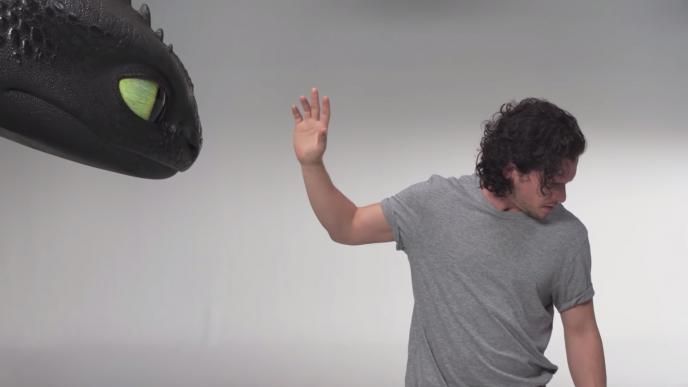 toothless the dragons face peaking through the left corner as actor kit harington holds his hand up and looks away from it