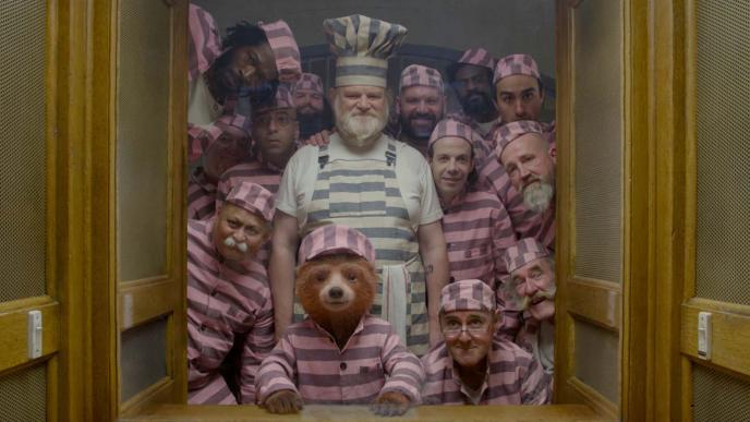 paddington bear wearing pink prison outfits with thirteen other prisoners. they are all peaking through a door