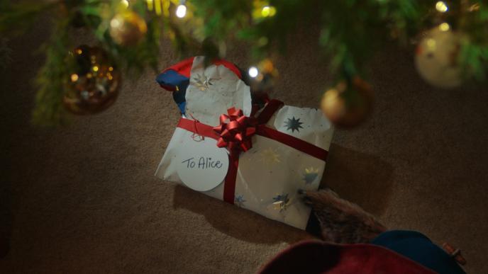 cg animated paddington bear putting a christmas present addressed 'to alice' under a christmas tree
