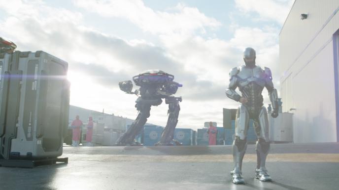 robocop standing on the right as an ed-209 enforcement droid stands in the background