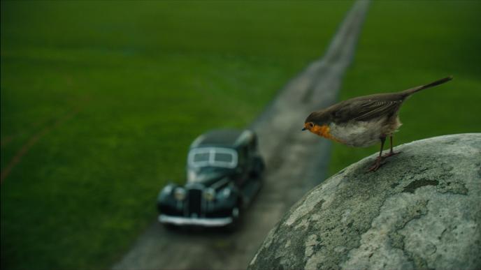 cg animated photorealistic robin standing on top of a statue looking down at a black 1950s somero car blurred into the background
