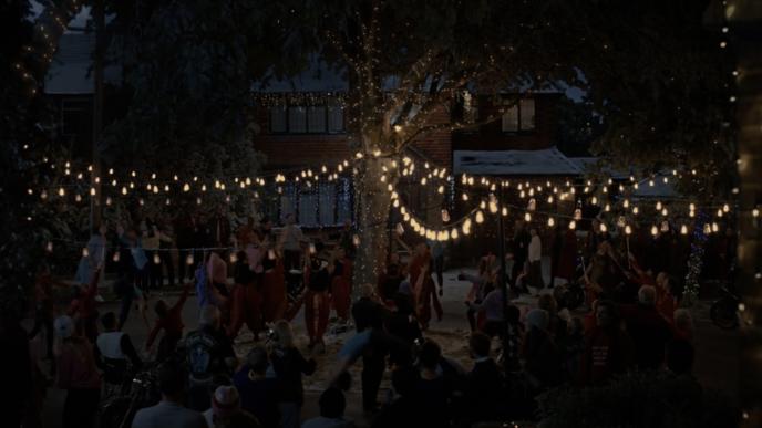 a group of people dancing and celebrating christmas under fairy lights attached to a tree