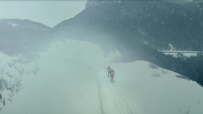 aerial shot of two people walking up a ski mountain in snow
