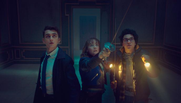 Lockwood and his friends hold up torches and weapons, in a dark room, looking upwards