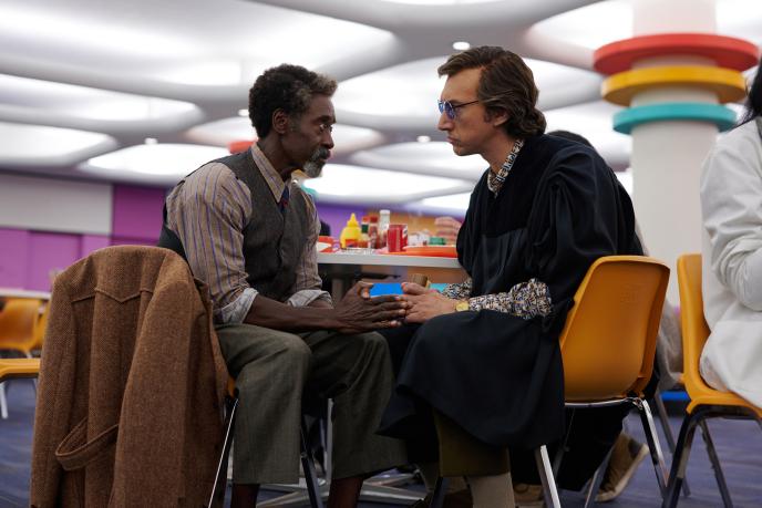 Two men sit facing each other, in a brightly coloured room, almost clasping hands.